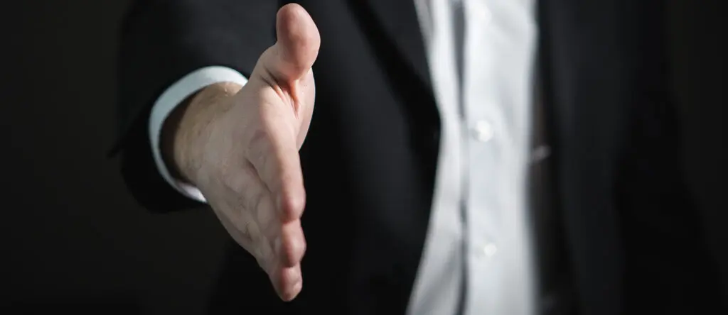 Hand reaching out for a handshake, symbolizing sales engagement and leadership connection in a professional setting.