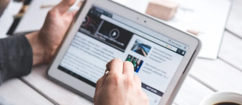 Person using a tablet to access digital resources related to sales enablement and leadership development, with a coffee cup in the foreground.