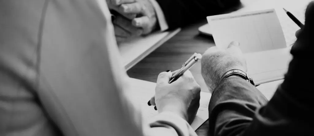 Hands writing notes and holding a pen during a business meeting, emphasizing leadership development and sales enablement discussions.