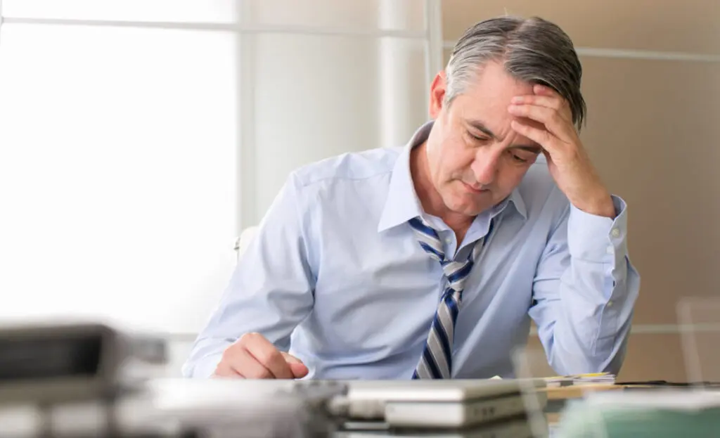 Frustrated business person with a disheveled tie, seated at a desk, reflecting on sales performance challenges and leadership development.