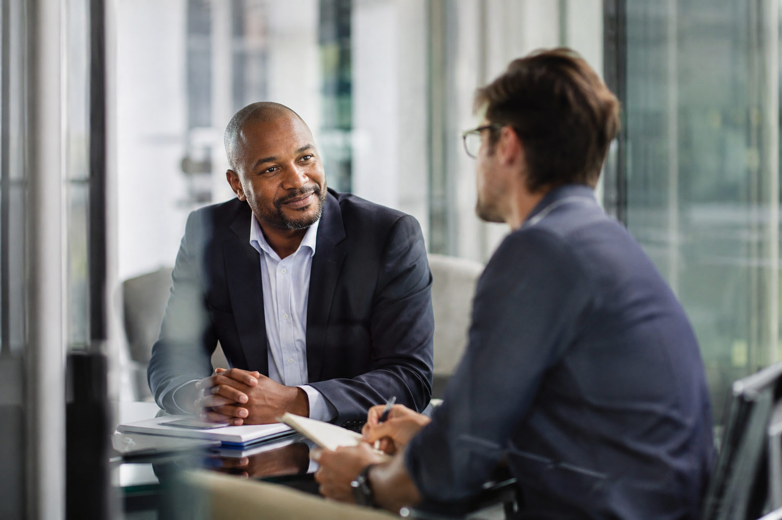 A senior leader smiles while coaching a rising manager one on one across a conference table, the kind of regular coaching cadence that builds real leadership readiness rather than a static talent list.